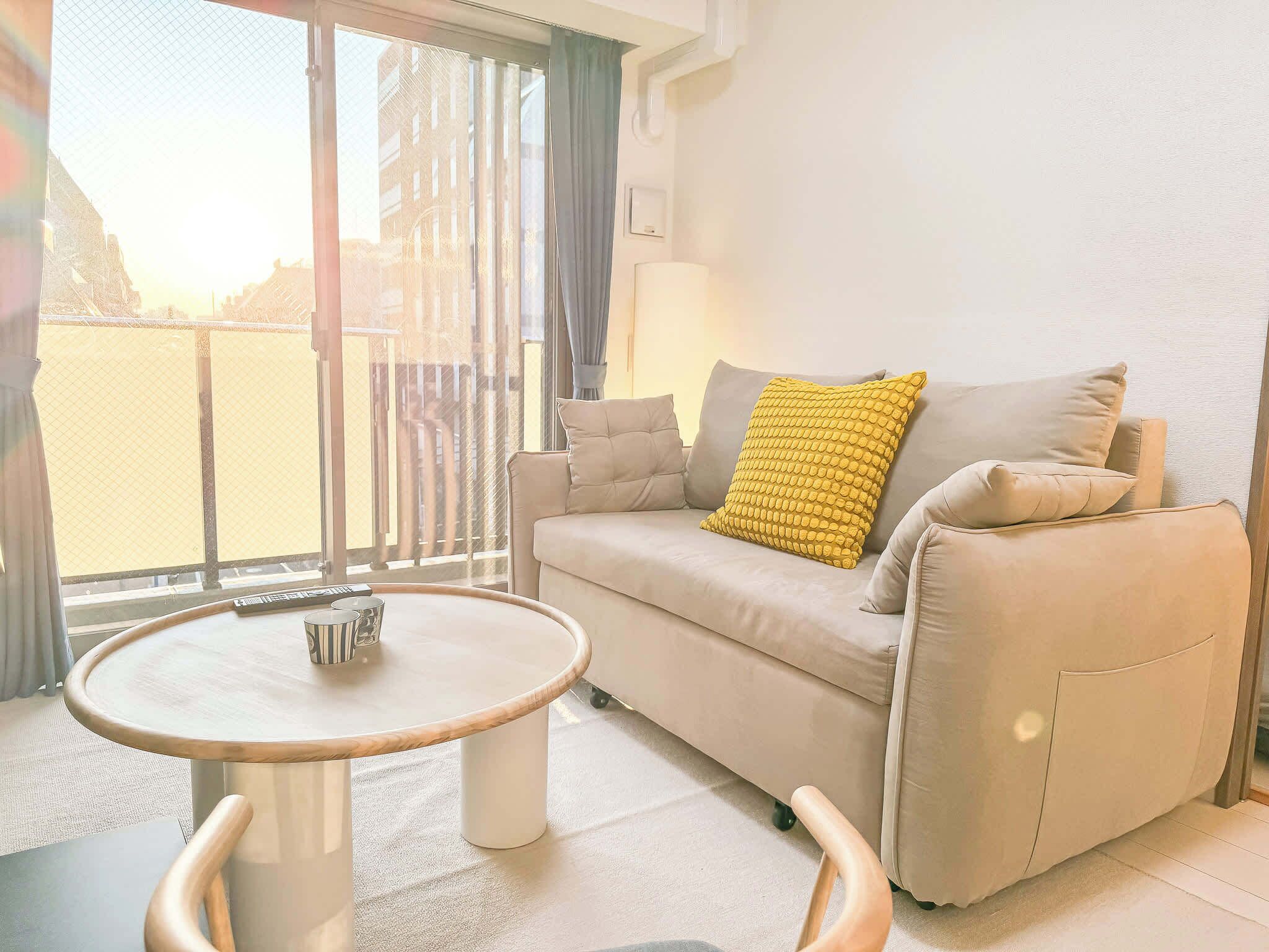A modern living room with a sofa, a round coffee table, and a view through a large window.