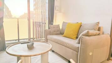 A modern living room with a sofa, a round coffee table, and a view through a large window.
