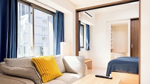 Ein modernes Hotelzimmer mit einer Couch, einem kleinen Holztisch, einem Bett und Blick auf die Stadt durch große Fenster.