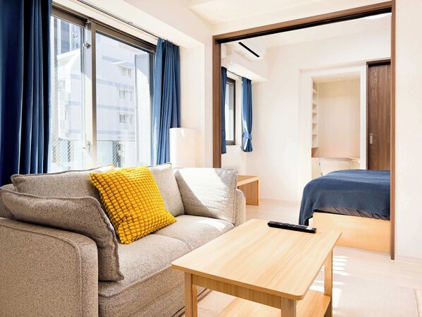 Ein modernes Hotelzimmer mit einer Couch, einem kleinen Holztisch, einem Bett und Blick auf die Stadt durch große Fenster.