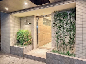A modern hotel entrance with a tiled facade, a wooden staircase, and a glass door leading inside. - Triphome Tokyo Sugamo 2024 New 3 mins 2 stations (Toshima City)