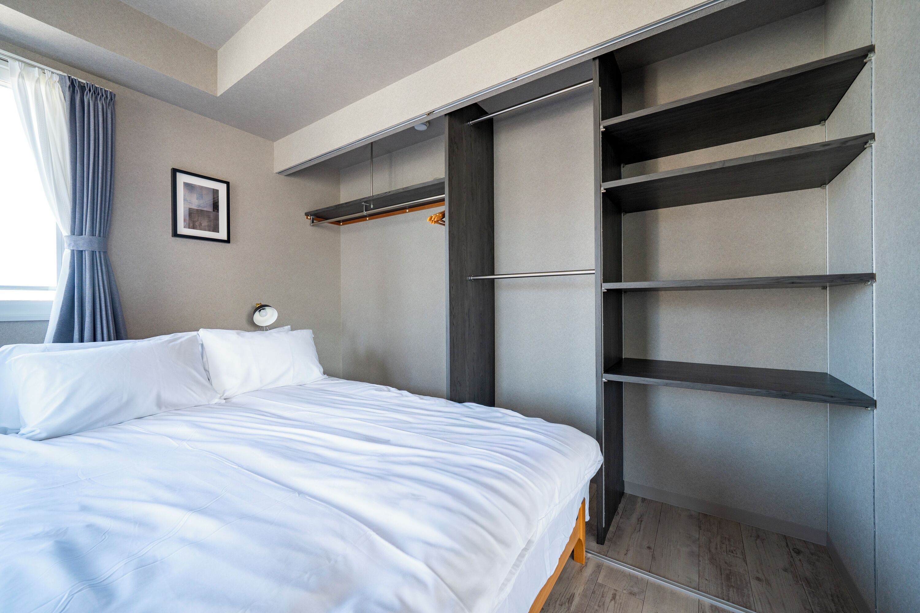 A bedroom with a bed, a wardrobe with shelves, a bedside table, and a window with curtains.