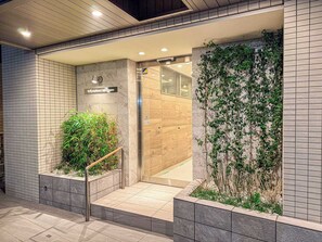 L’entrée d’un hôtel moderne, avec une façade carrelée, un escalier en bois et une porte en verre donnant sur l’intérieur.
