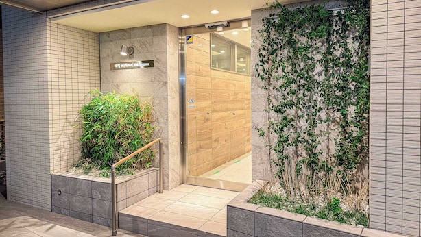 L’entrée d’un hôtel moderne, avec une façade recouverte de carreaux, un escalier en bois et une porte en verre donnant sur l’intérieur.
