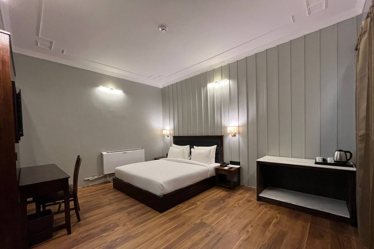 A modern hotel room with a large bed, bedside tables, a desk, and a built-in bench.
