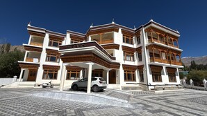 A multi-story building with balconies, a covered entrance, and a paved driveway. - Hotel Raks  (Leh)