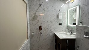 A modern bathroom with a marble wall, a sink, a mirror, and a shower. - Hotel Raks  (Leh)