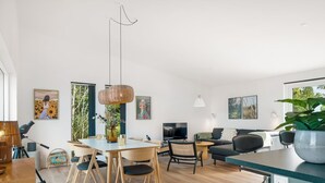 Een moderne woonkamer met een eethoek, met een groot raam, een flatscreen televisie en een potplant.
