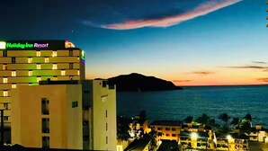 A Holiday Inn Resort building with a view of the ocean and a sunset. - Luxury apartment with ocean view in the golden zone (Mazatlán)