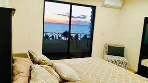 A bedroom with a large window overlooking a balcony with a view of the sea and sunset. - Luxury apartment with ocean view in the golden zone (Mazatlán)