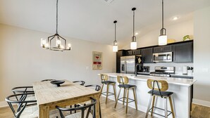 Cozinha moderna com ilha central, eletrodomésticos de aço inoxidável e iluminação pendente.