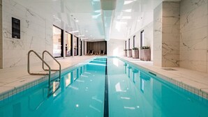 Una piscina interior con agua cristalina, rodeada de paredes de mármol e iluminación empotrada en el techo.