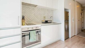 Une cuisine moderne avec des meubles blancs, un dosseret en motif chevrons, un réfrigérateur en acier inoxydable et un four encastré.