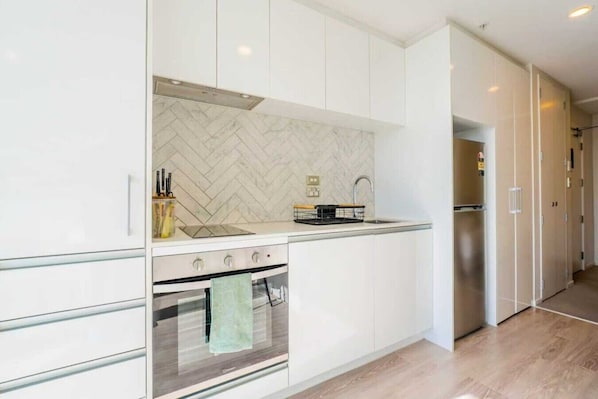 A modern kitchen with white cabinetry, a herringbone backsplash, a stainless steel refrigerator, and a built-in oven.