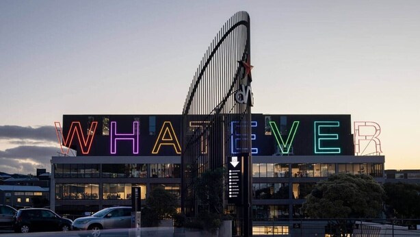 Un edificio con un letrero iluminado de neón grande que dice 'WHATEVER'.