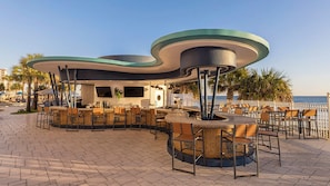 An outdoor bar area with a curved roof, seating, and a view of the sea.