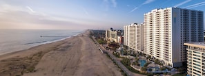 A coastal hotel with multiple high-rise buildings, a beach, and a pier.