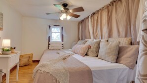 Ein Schlafzimmer mit einem Bett, einem Schreibtisch mit Lampe, einem Deckenventilator und einem Fenster mit Vorhängen.