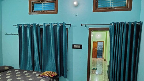 Quarto com cama, cortinas e porta que dá para outro cômodo.