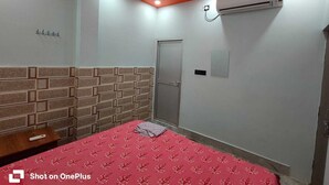 Um quarto com cabeceira em padrão de tijolos, cama com colcha floral vermelha, ar-condicionado e ventilador de teto.