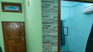Um corredor com porta de madeira, parede de pedra, cama com colcha de bolinhas e aparelho de ar condicionado.