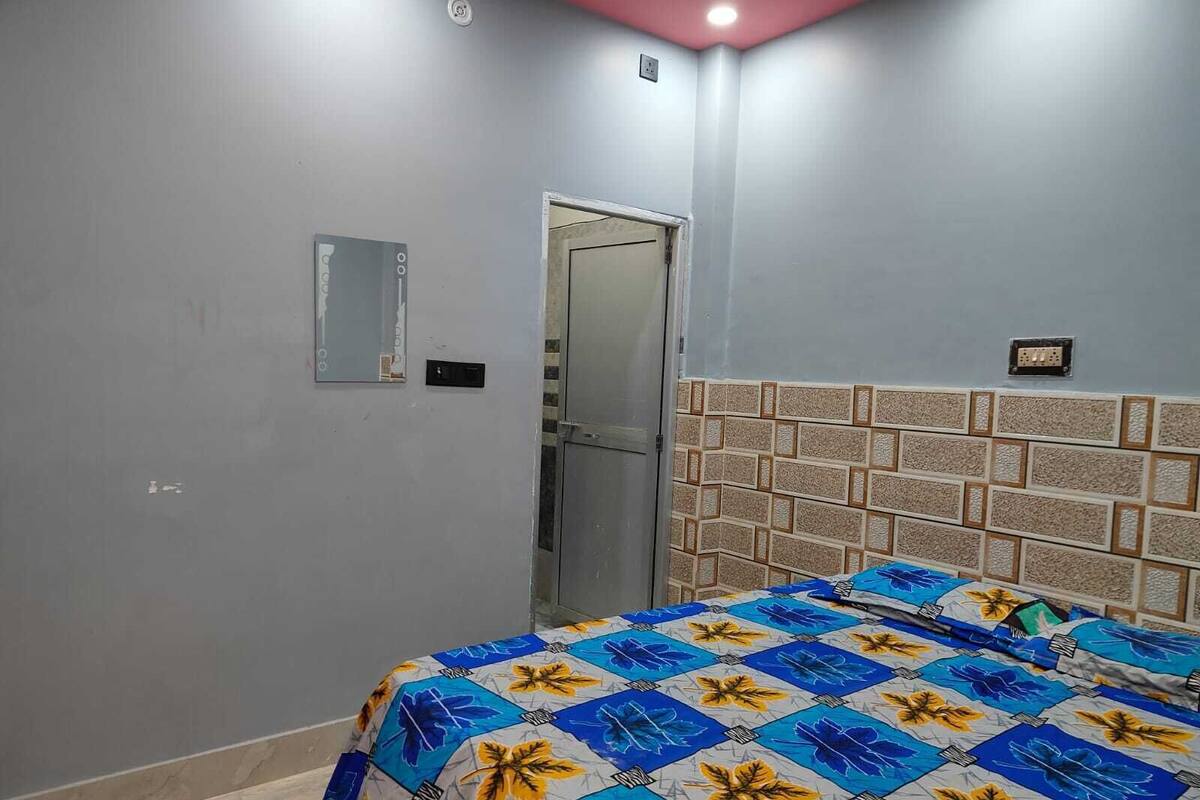 Un dormitorio con cama, una puerta, una lámpara fijada a la pared y un enchufe.