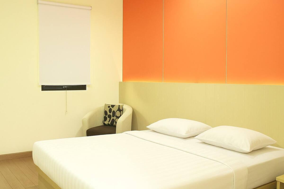 Ein Hotelzimmer mit einem Bett, einem Sessel, einem weißen Kopfkissen und einer Wand-Klimaanlage.
