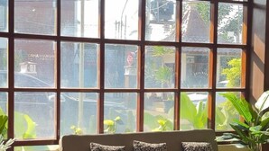 A room with a large window, a sofa with patterned cushions, and a potted plant. - Hotel Setia Budi Madiun (Madiun)
