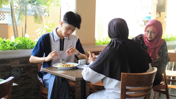 A dining area with a table set for two people, one person eating and the other holding a phone.