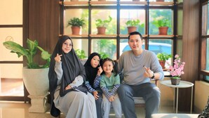 A family sitting indoors with a large potted plant and a small table with a flower pot. - Hotel Setia Budi Madiun (Madiun)