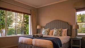 A bedroom with a large bed, two bedside tables, and a view of trees through the window. - Hermanus Family Getaway - Near The Beach (Hermanus)