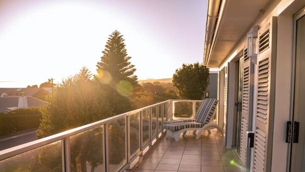 A balcony with a view of trees and a road, a chair, and a railing. - Hermanus Family Getaway - Near The Beach (Hermanus)