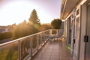 A balcony with a view of trees and a road, a chair, and a railing. - Hermanus Family Getaway - Near The Beach (Hermanus)