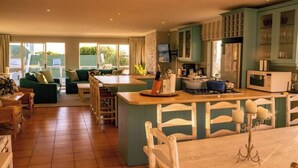 A spacious living area with a kitchen island, green sofas, and a dining table with chairs. - Hermanus Family Getaway - Near The Beach (Hermanus)