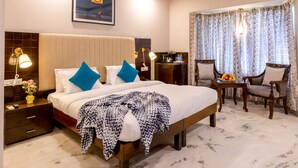 A hotel room with a bed, bedside tables, a desk, chairs, a ceiling fan, and a window with curtains.