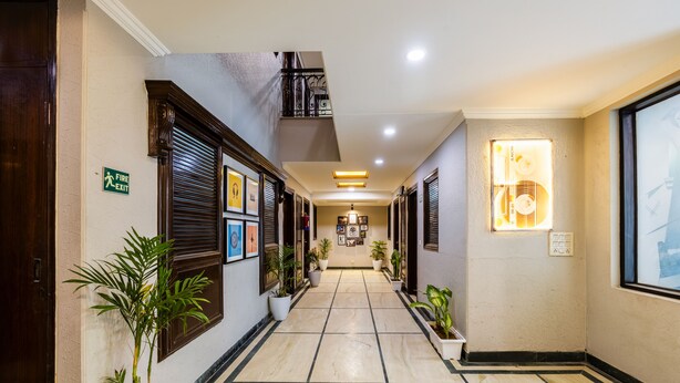 A hotel hallway with a fire exit sign, potted plants, and framed pictures on the walls.