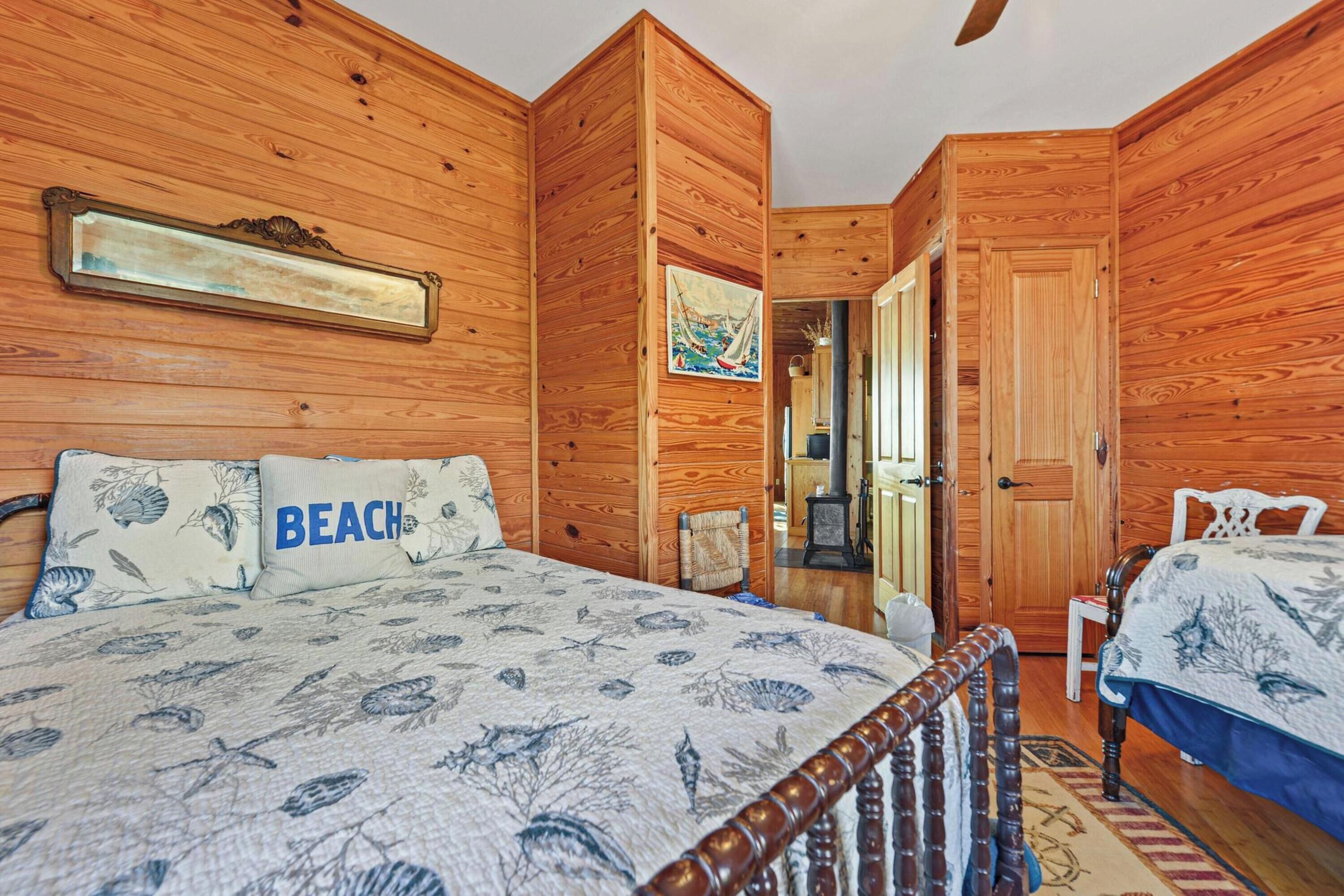 Een houten kamer met een bed, een stoel en een deur naar een andere kamer.