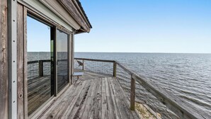 A wooden deck with a glass door leading to a room, overlooking a calm body of water.