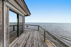 A wooden deck with a glass door leading to a room, overlooking a calm body of water. - Rustic Retreat (Ocean Springs)