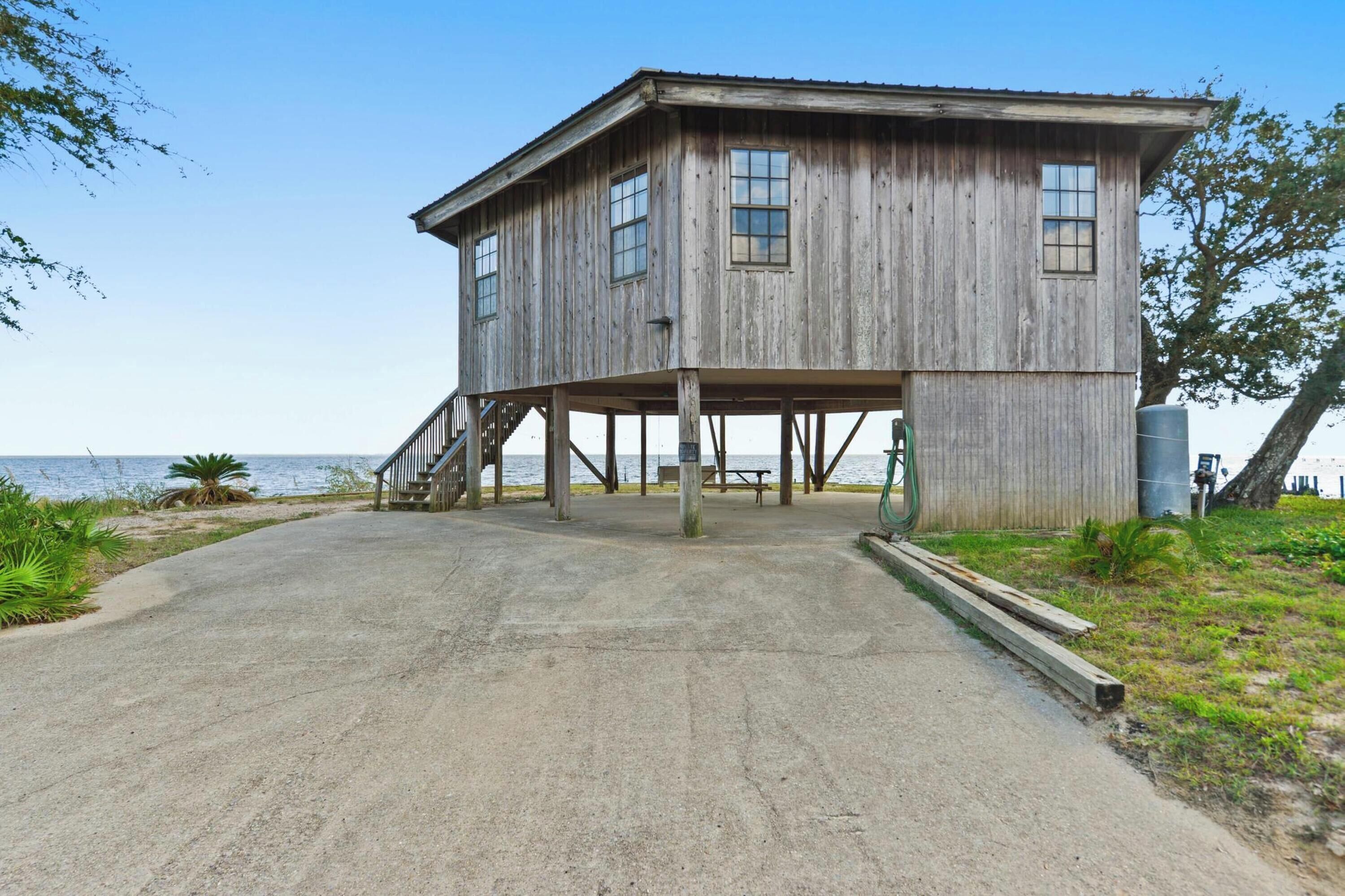 Une maison en bois dotée d’un porche et d’un escalier menant à l’entrée, située près d’une étendue d’eau.