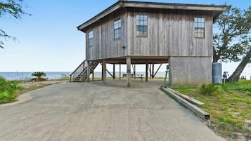 Une maison en bois dotée d’un porche et d’un escalier menant à l’entrée, située près d’une étendue d’eau.