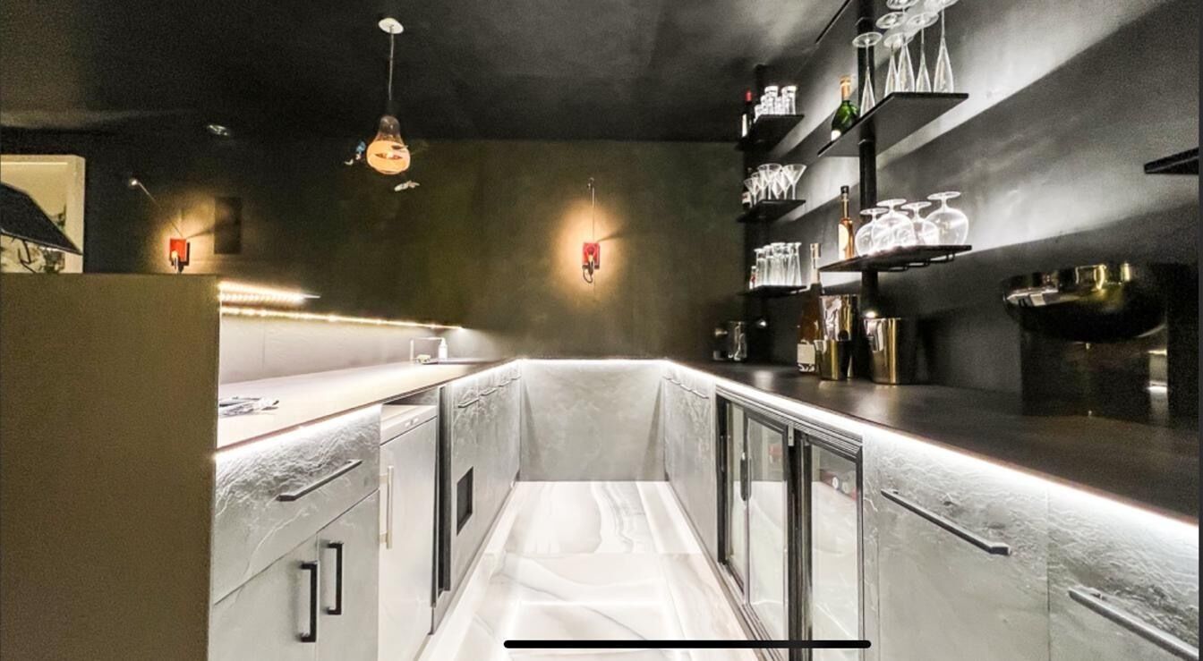 Eine schmale, moderne Küche mit Edelstahlgeräten, einer Glastrennwand und einer Bar mit Regalen voller Gläser und Flaschen.