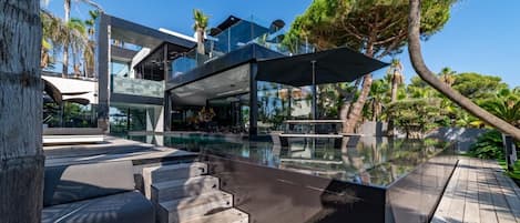 A modern pool area with a glass-enclosed structure, outdoor seating, and lush tropical landscaping.