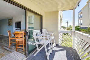 A balcony with a table and chairs, a sliding glass door, and a view of a building and palm tree. - Direct Beach Access! Walkable Condo on Ocean Blvd (North Myrtle Beach)
