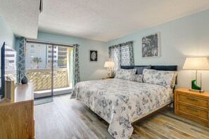 A bedroom with a bed, nightstands, a dresser, a window with curtains, and a view of buildings outside. - Direct Beach Access! Walkable Condo on Ocean Blvd (North Myrtle Beach)
