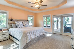 A bedroom with a bed, a nightstand, a dresser, a ceiling fan, and large windows. - Boat, Fish & Explore! Gem on Lake of the Ozarks (Roach)