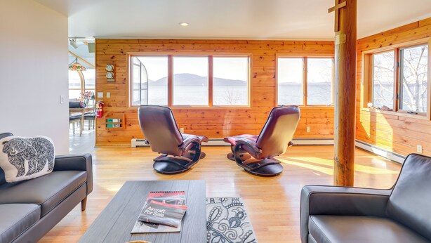 Una sala de estar moderna con un ventanal grande que da a una masa de agua, paredes de madera y dos sillones de cuero.