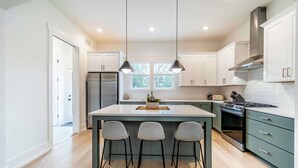 Una cocina moderna con una isla central, taburetes de bar, electrodomésticos de acero inoxidable y vistas al exterior.
