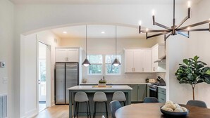 Una cocina moderna con una isla central, iluminación colgante y un comedor con mesa y sillas de madera.