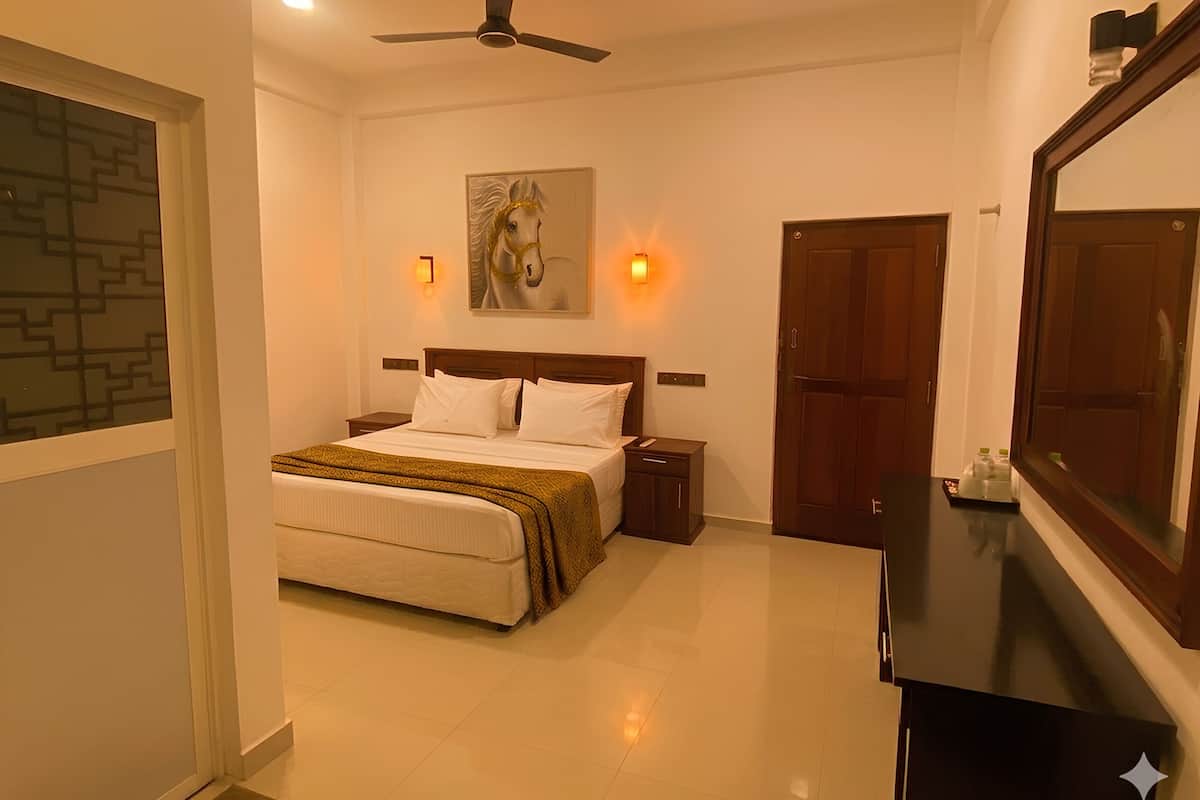 Una habitación de hotel con cama, mesitas de noche, ventilador de techo, un cuadro, apliques de pared, espejo y armario.